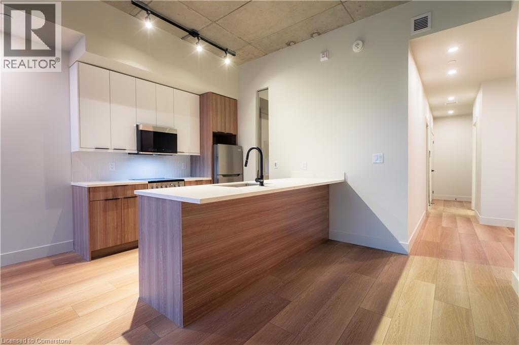 24 AUGUSTA Street Unit# 208=Kitchen with brown cabinets, rail lighting, modern cabinets, and light wood-style floors